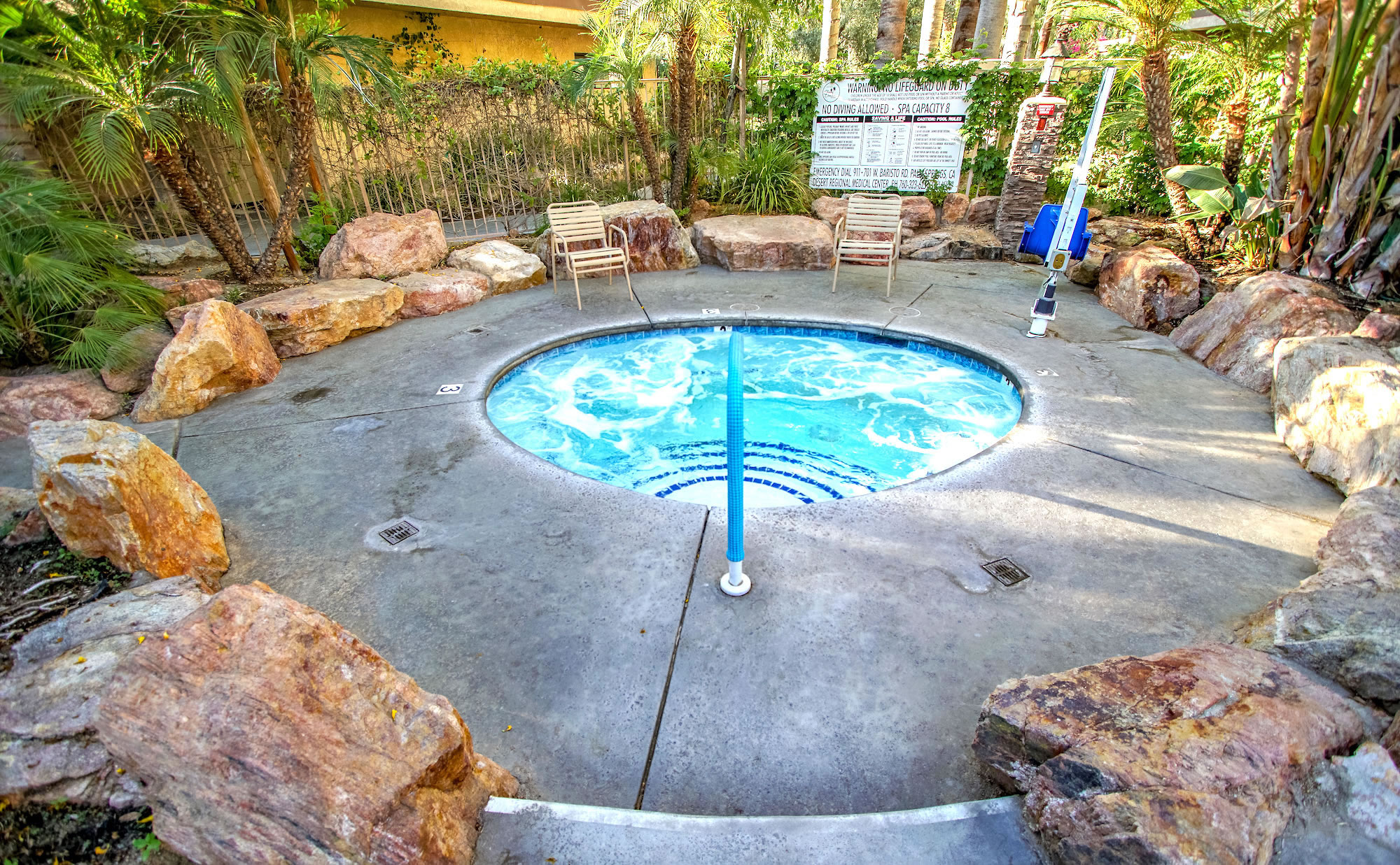 A circular hot tub with bubbling water, surrounded by large rocks and palm trees.