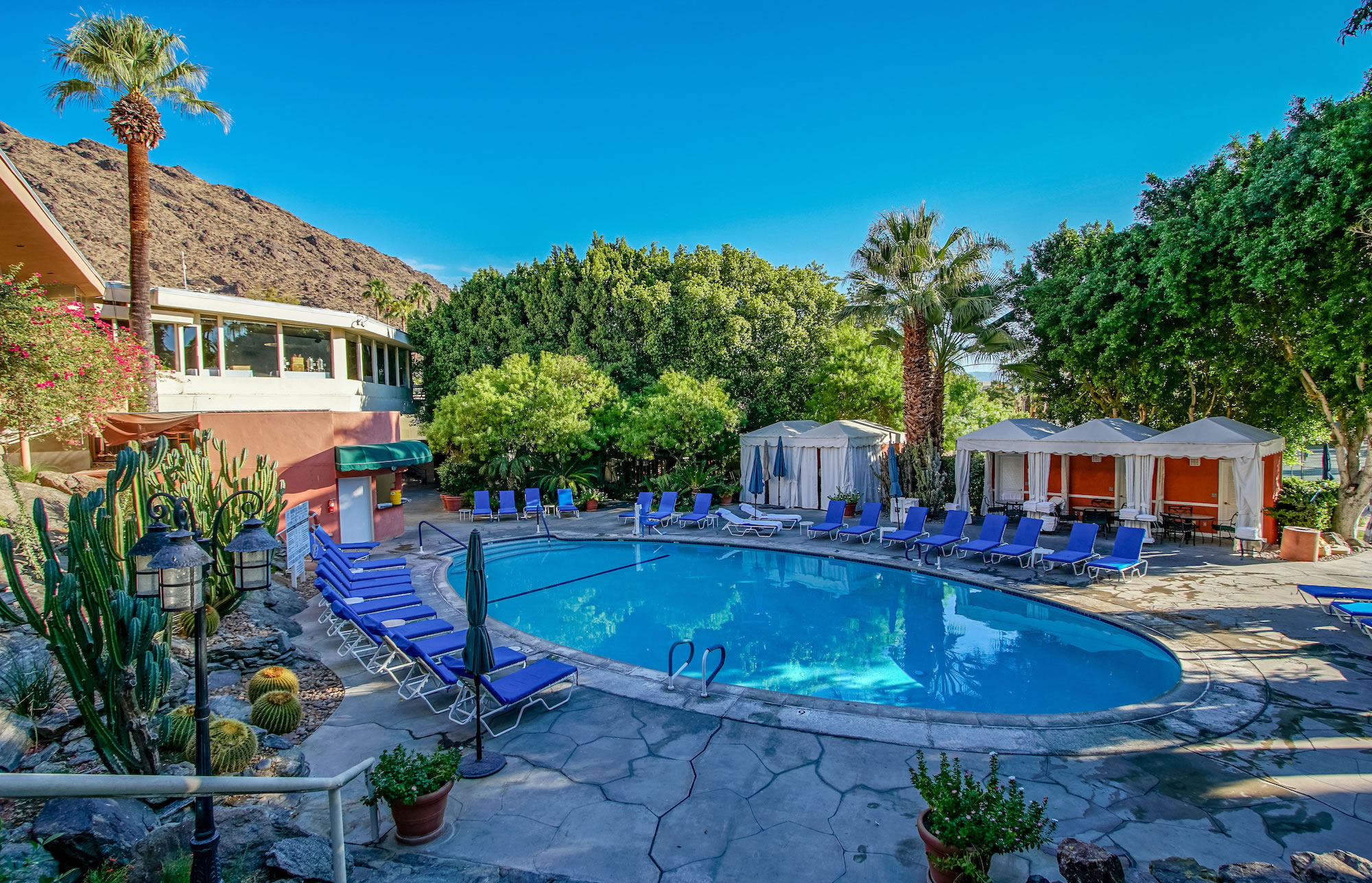 A resort pool with blue lounge chairs and a cabana in the background.