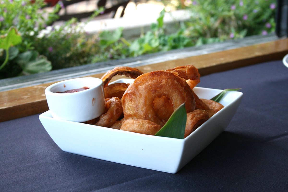 A plate of fried food with dipping sauce on a table with a garden view.